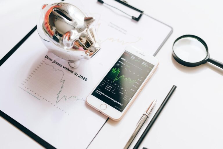 Flat lay of financial tools: chart, smartphone, magnifying glass, and piggy bank.